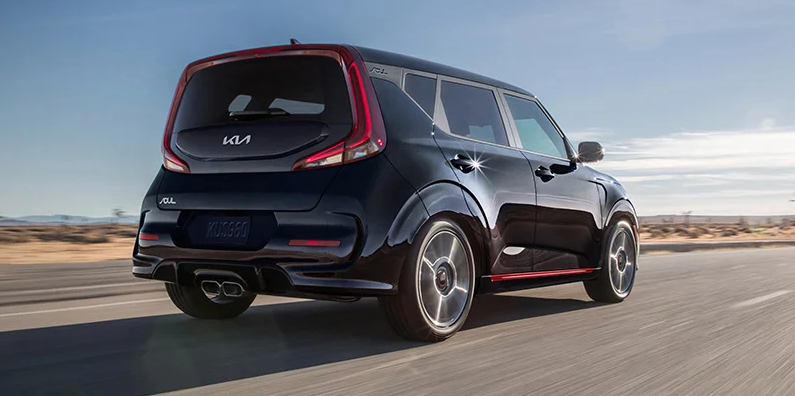A black Kia Soul driving down the road.